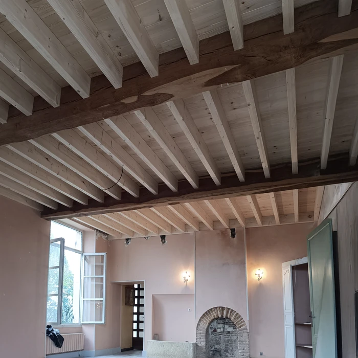 Intérieur en cours de rénovation avec plafond à poutres apparentes en bois naturel