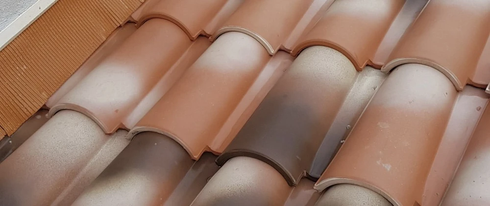 Extérieur d'une toiture avec tour pyramidale en ardoises grises, cheminée en briques rouges et tuiles canal en terre cuite