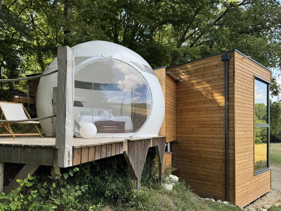 Scène extérieure montrant une micro-maison mobile sur remorque avec terrasse en bois, stationnée sous des arbres